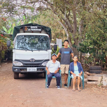 Three people sitting in front of a white truck with a green cover in a rural setting.